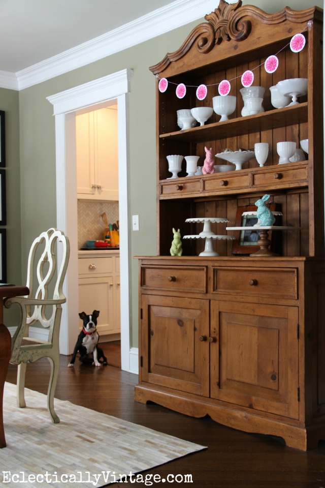 Love all the white milk glass in the pine hutch - the DIY flower banner is perfect for spring kellyelko.com