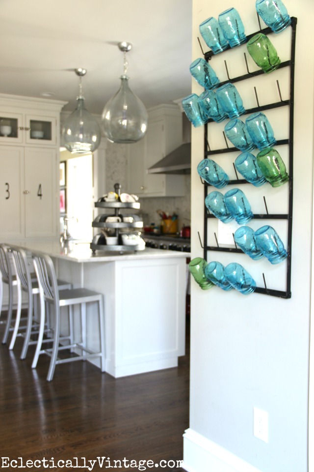 This wall bottle drying rack is huge and so cool! I love the way she used it to display colorful mason jars and she shows other creative ways to style it plus where to buy it! kellyelko.com #farmhouse #farmhousedecor #farmhousekitchen #platewall #vintagedecor #vintagekitchen #eclecticdecor #colorfuldecor #masonjars #cottagedecor #whitekitchen 
