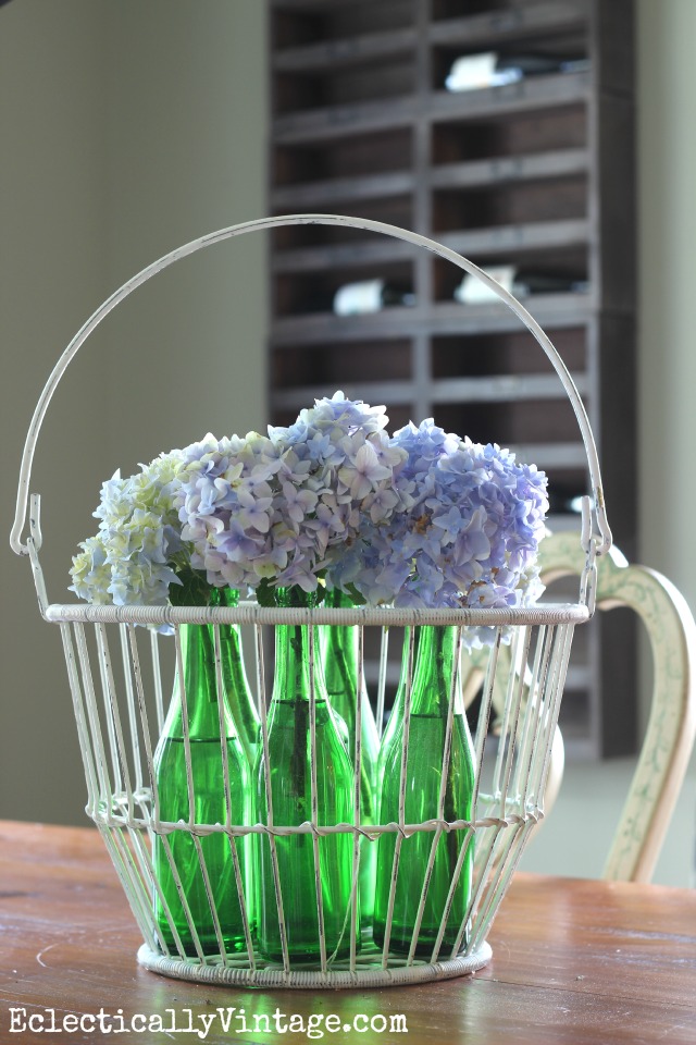 Beautiful hydrangea centerpiece in a collection of old glass bottles in a wire basket kellyelko.com