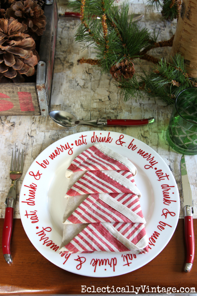 Rustic and whimsical Christmas tablescape. Love the napkin folded into the shape of a tree, birch bark table runner and red plates and cutlery kellyelko.com