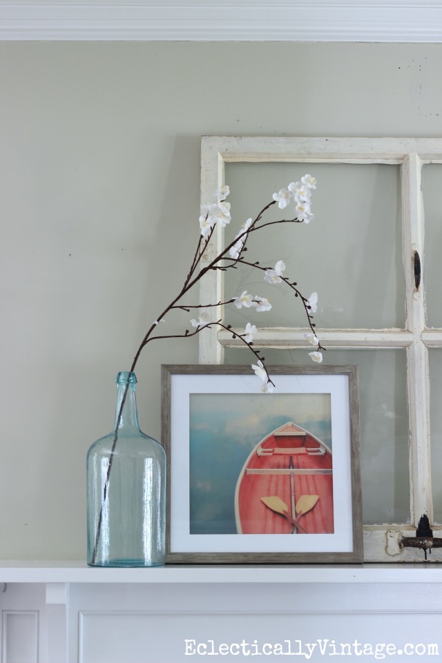 Prop and layer accessories on the mantel for a relaxed look. Love the boat art and the old green bottle holding a single flowering branch kellyelko.com